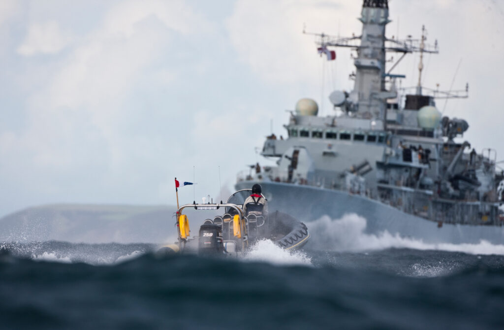 Commercial RIB charter operating in heavy seas alongside a naval warship, providing professional offshore support and high-speed marine operations in UK waters.