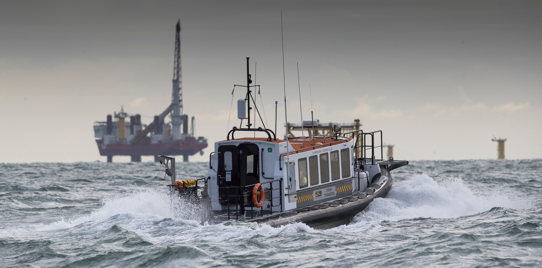 Commercial RIB crew transfer vessel operating in rough seas near offshore wind construction infrastructure, supporting safe personnel transfer.