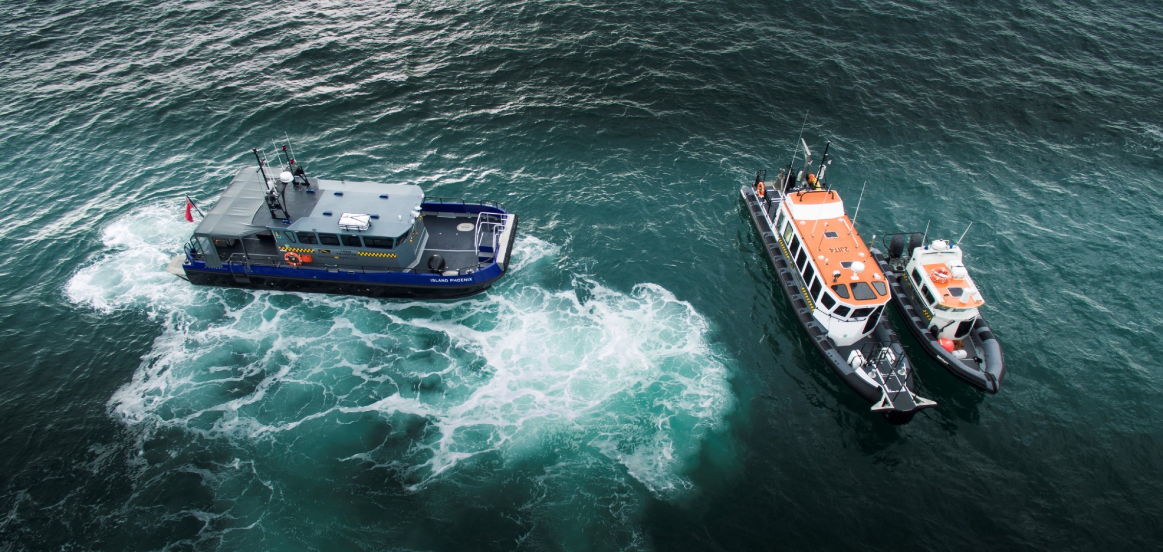 Aerial view of commercial RIB crew transfer vessels operating alongside a workboat offshore, delivering marine safety cover and personnel transfer support.