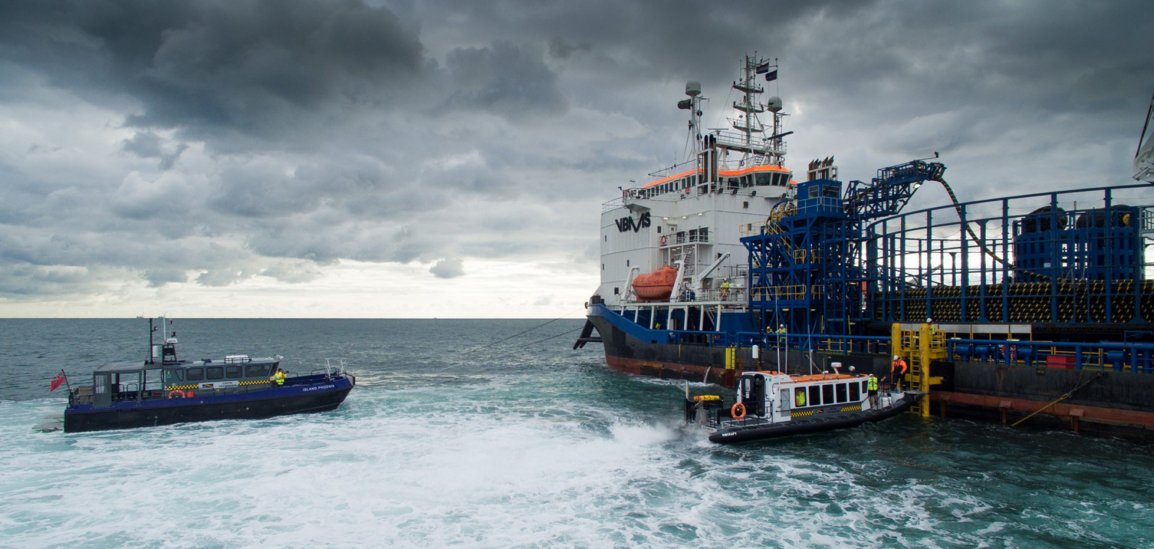 Commercial RIB crew transfer and safety vessels operating alongside an offshore construction ship in heavy weather, providing marine support, personnel transfer, and standby safety services.