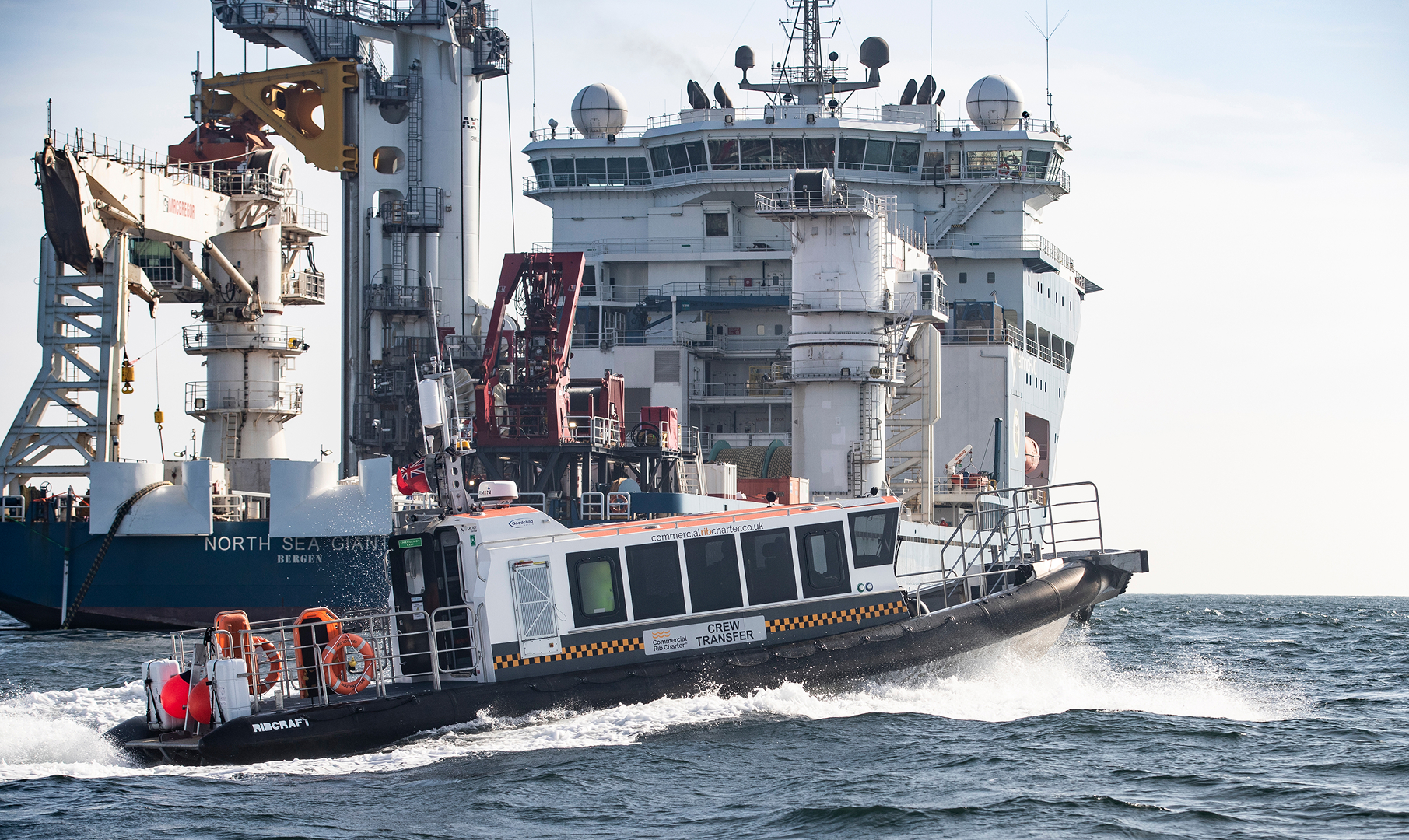 Commercial RIB charter vessel conducting offshore crew transfer alongside a large offshore construction vessel.